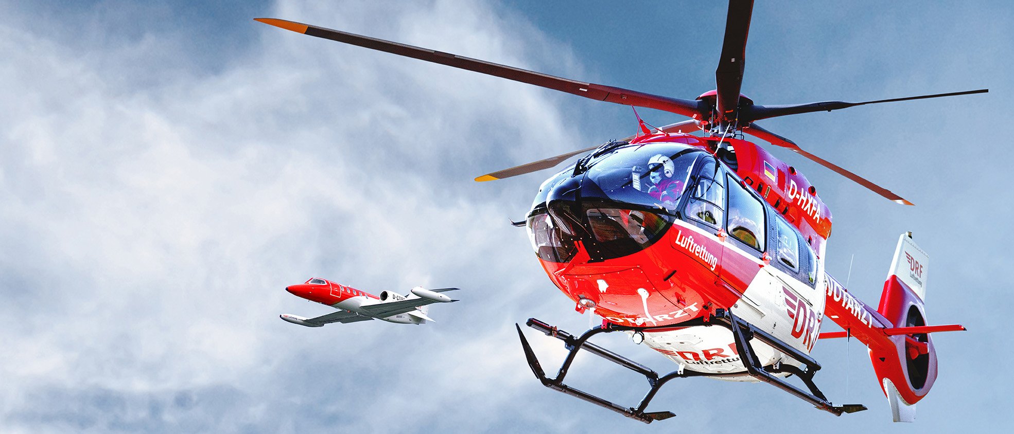 Hubschrauber und Learjet der DRF Luftrettung im Flug vor blauem Himmel