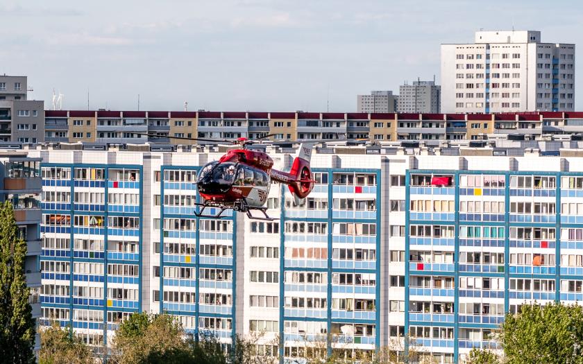 Ein rot-weißer Hubschrauber schwebt vor einem mehrstöckigen Wohnhaus mit blau-weißer Fassade