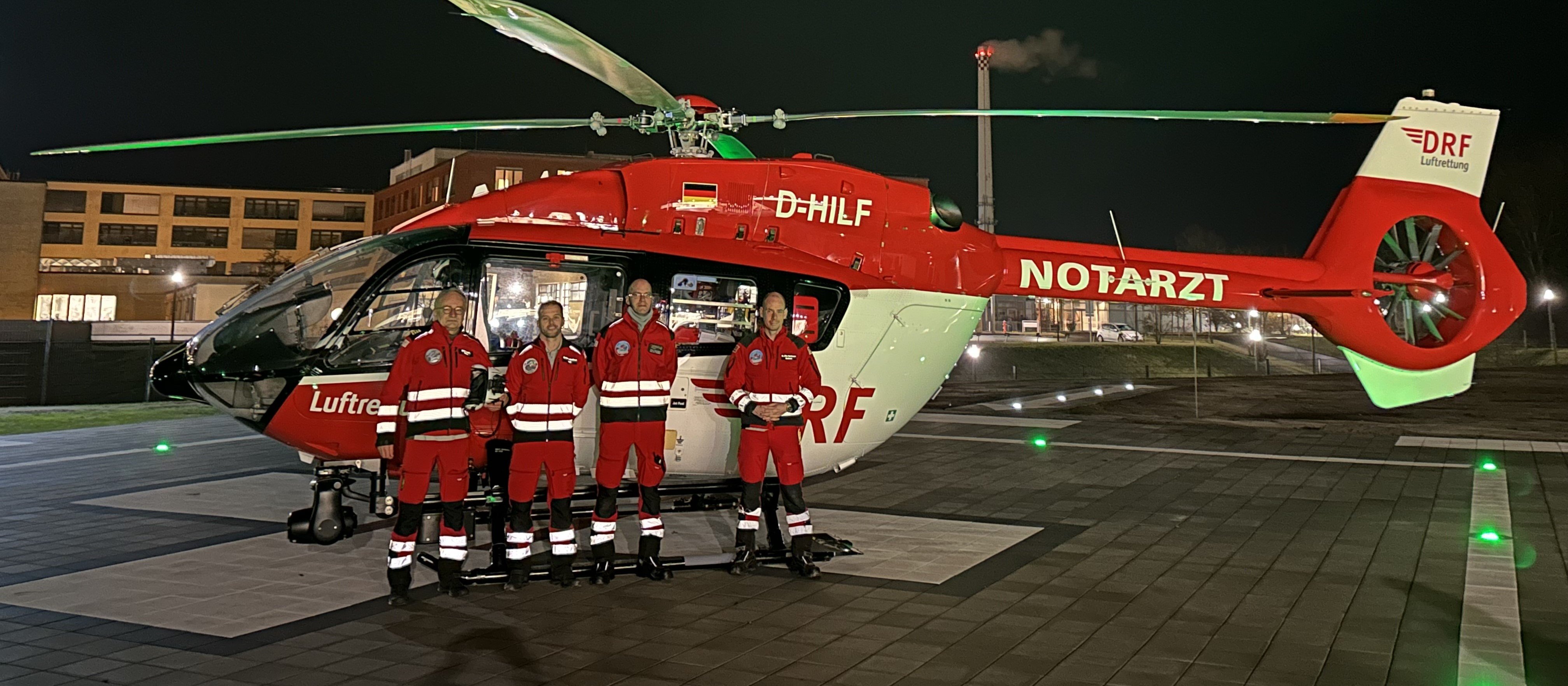 Eine vierköpfige Crew steht vor einem rot-weißen Hubschrauber