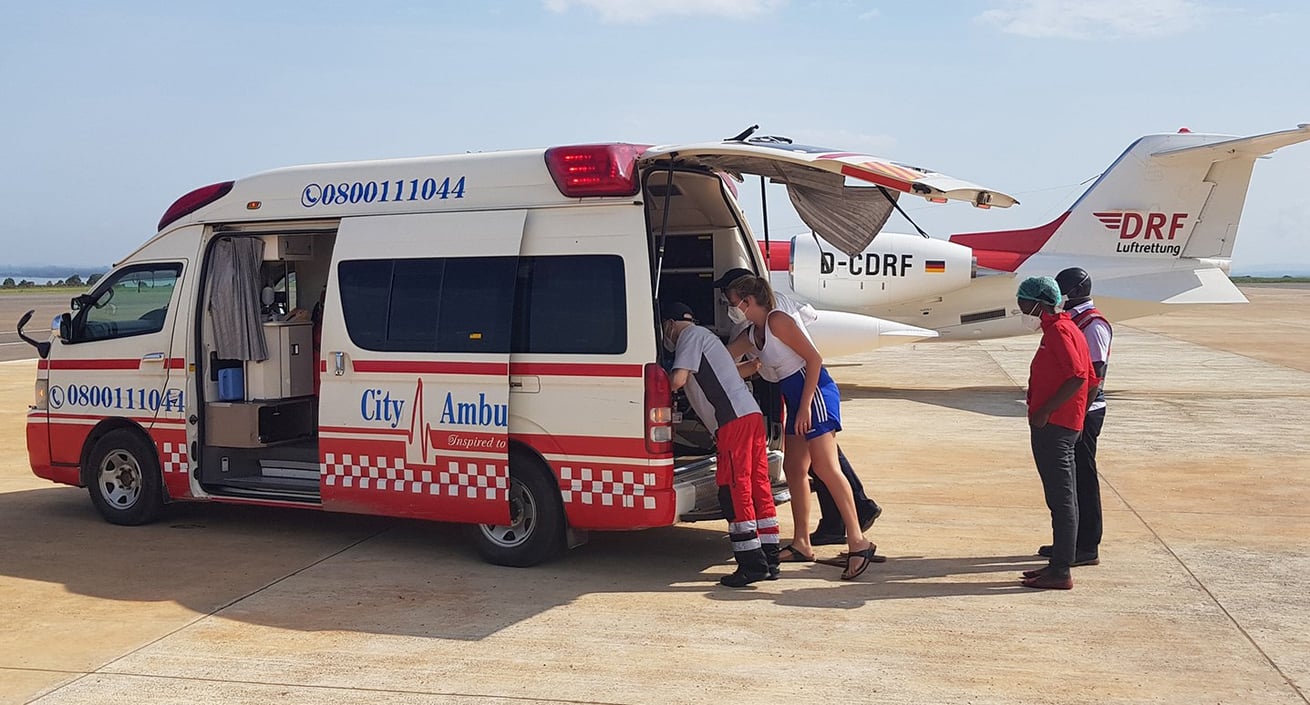Patient und Krankentransportwagen erreichen das Flugzeug; Dr. Johannes Meyer bei der Begutachtung des Patienten