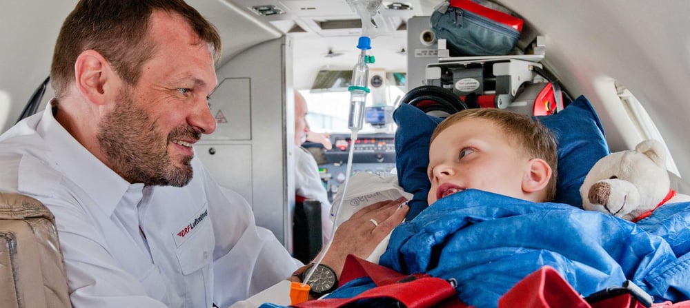Ein Junge liegt auf der Trage eines Ambulanzflugzeugs und wird von einem Notfallsanitäter betreut