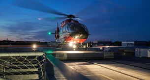 Ein Hubschrauber steht mit drehenden Rotoren in der Dämmerung auf einem Landeplatz
