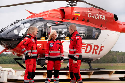 Eine Crew eines Rettungshubschraubers steht vor einem rot-weißen Hubschrauber