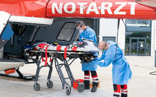 Zwei Männer in Vollschutz desinfizieren eine Patiententrage, die am offenen Heck eines Hubschraubers steht.